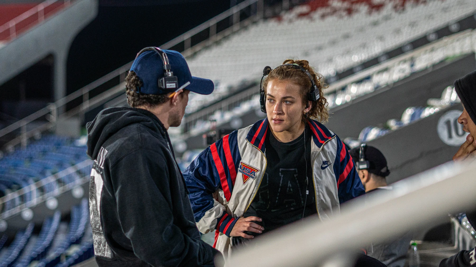 El director de espaldas conversando con el equipo en las tribunas del estadio de noche